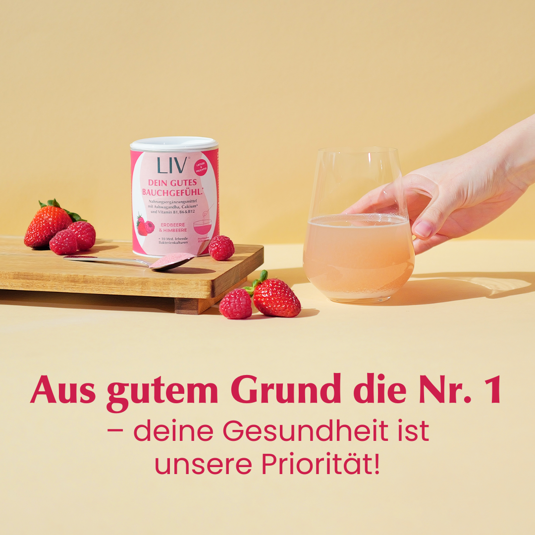 Verpackung der Darmkur auf einem Holzbrett mit Erdbeeren und Himbeeren davor. Ein Löffel mit rosa Pulver liegt vor der Darmkur, während neben dem Holzbrett ein Glas mit rosa Flüssigkeit steht.